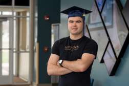 Mick smiling while wearing his graduation cap and his arms crossed.