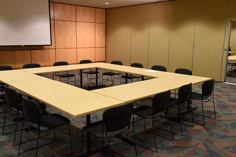A large training room with the wall closed, dividing the training room into two. Tables are set up in a square pattern, with 4 chairs on each side.