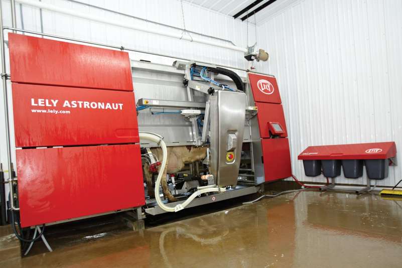 A large red milking machine sits in the corner of the shed. A cow is inside it being milked.