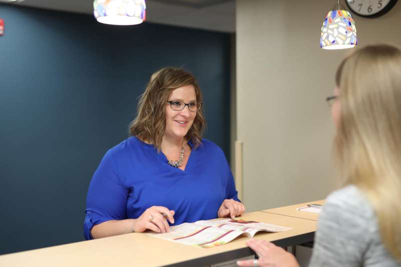 Woman stands at a lobby desk, getting information from a staff member.