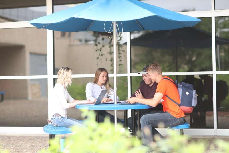 Four students sitting at a picnic table in the courtyard of the Wausau campus.