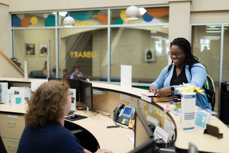 A student standing at the front desk, getting information from the library staff.
