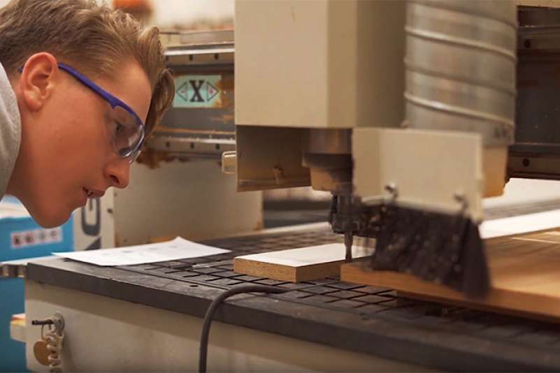 A student inspects his work on a woodworking machine