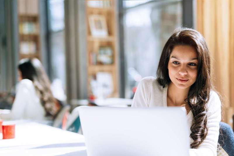 A young professional woman sitting at a table with a laptop in front of her.