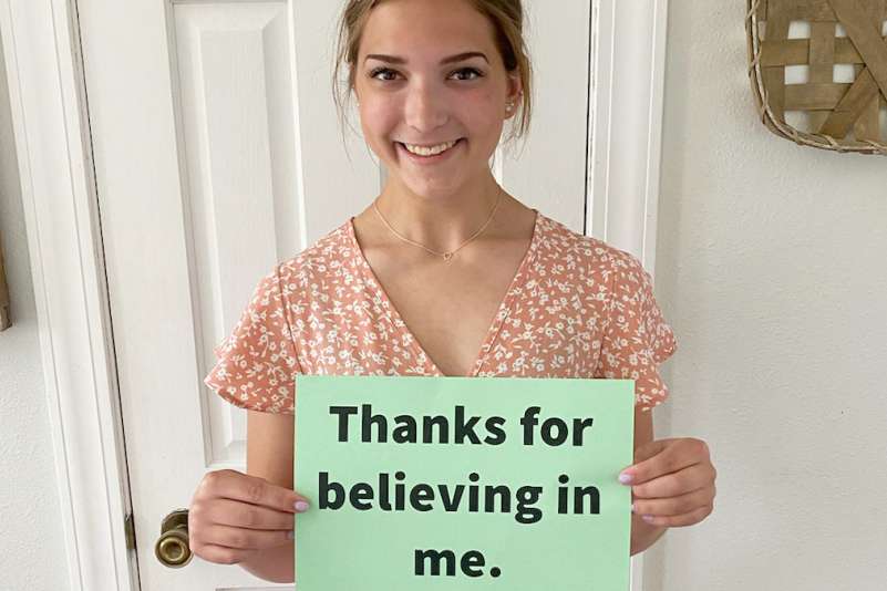 An NTC student holds up a small sign with "Thanks for believing in me" written on it.