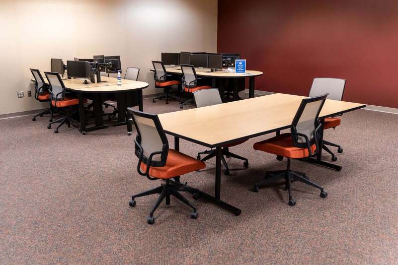 Three work tables within the Community Technology Center, two of which have desktop computers available for use.