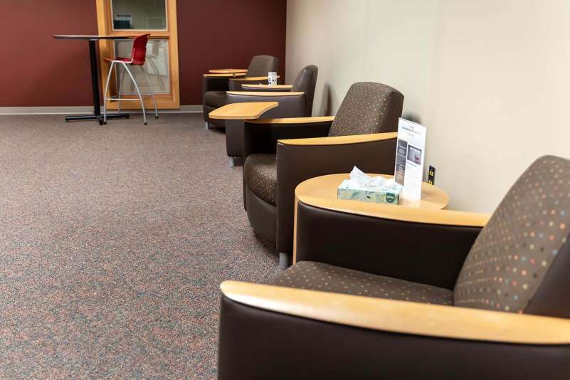 Several soft seating chairs along a wall in the Community Technology Center, along with one high-top work table.