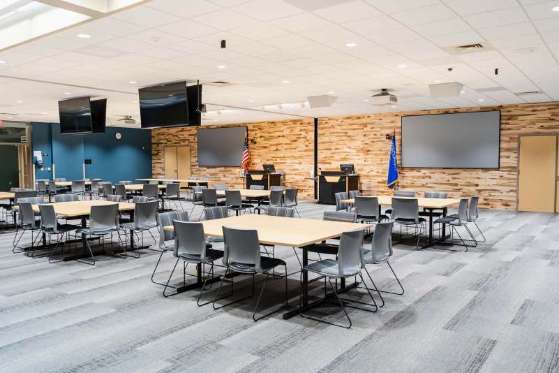 The E101 & E102 conference rooms with the dividing wall opened up, showing a square table configuration with 8 chairs at each table.