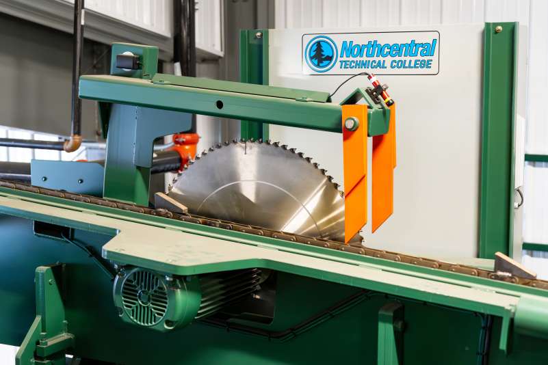 Close-up of a large circular saw blade mounted in a green and orange machine, part of Northcentral Technical College’s sawmill training facility.