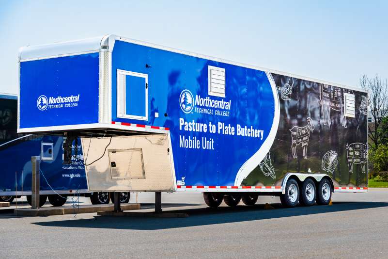 The Pasture to Plate mobile lab trailer, as seen from a front angle view. Diagrams of butchery cuts adorn the side of the trailer.