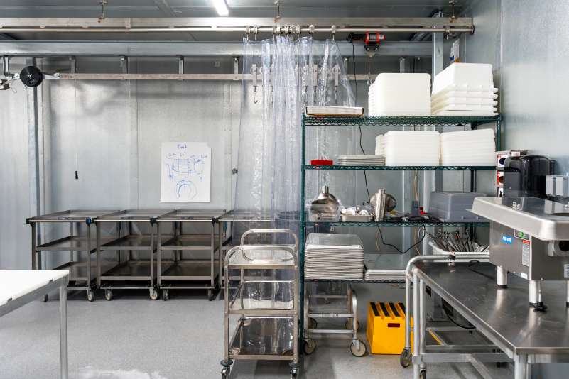 The Cold Lab: a sterile industrial kitchen with stainless steel carts, shelving units holding supplies, and a hanging rack.