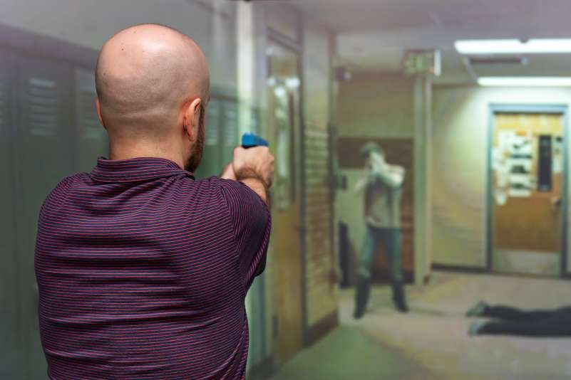 Man aiming mock handgun down school hallway toward armed intruder by lockers