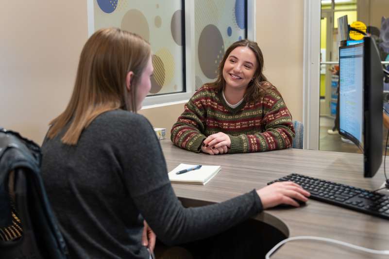 A student smiling while talking with an advisor at her desk