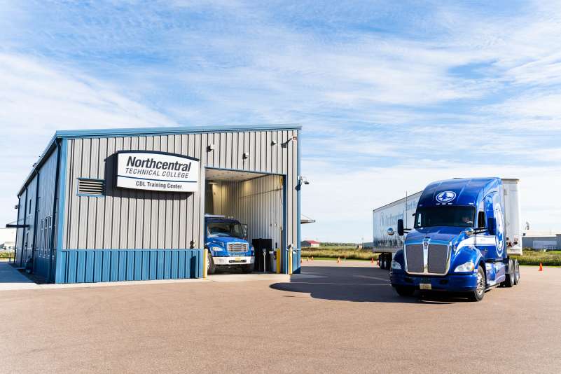 An NTC truck pulling around the front of the CDL Training Center, while another truck sits in the open bay.