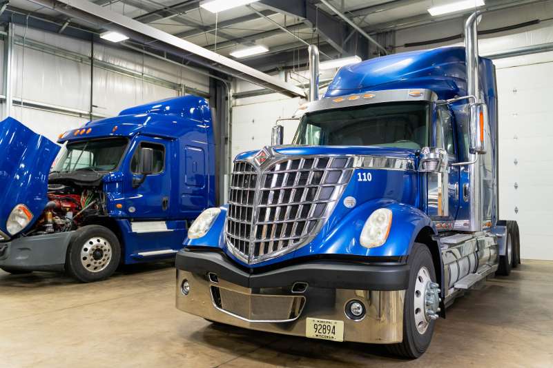 Two blue semi truck cabs inside the Diesel Technology Center, one with its hood open.