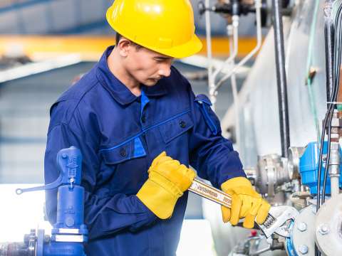 A student wearing a blue jumpsuit and a yellow hardhat is tightening a bolt with a wrench