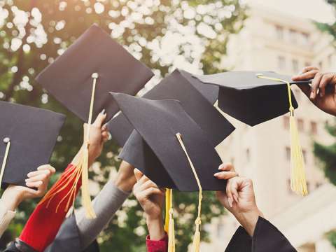 Several students are holding up their graduation hats