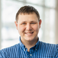 Logan Wells, smiling while standing in front of a wall of windows.
