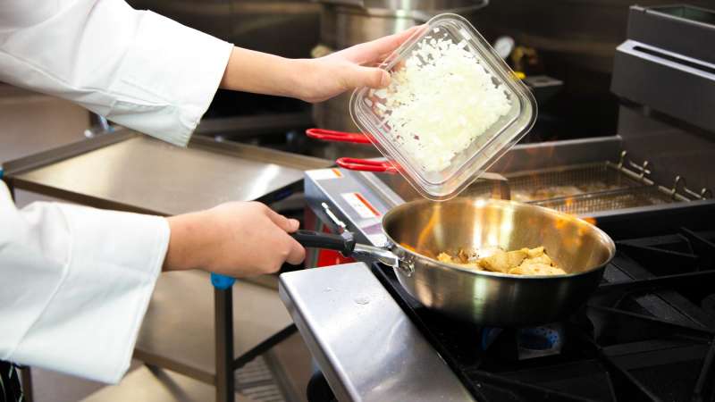 Chef pouring chopped onions into a flaming pan held over a stove