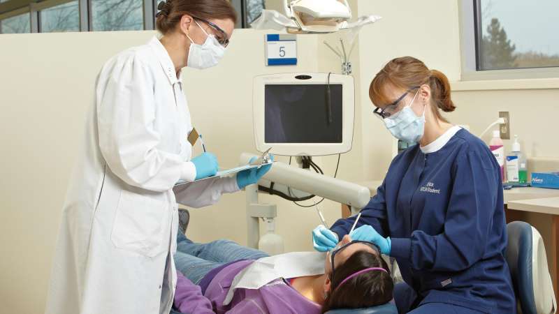 Dental student working on a patient with the instructor nearby