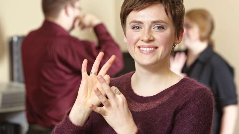 Sign language interpreter signing with people standing behind her.