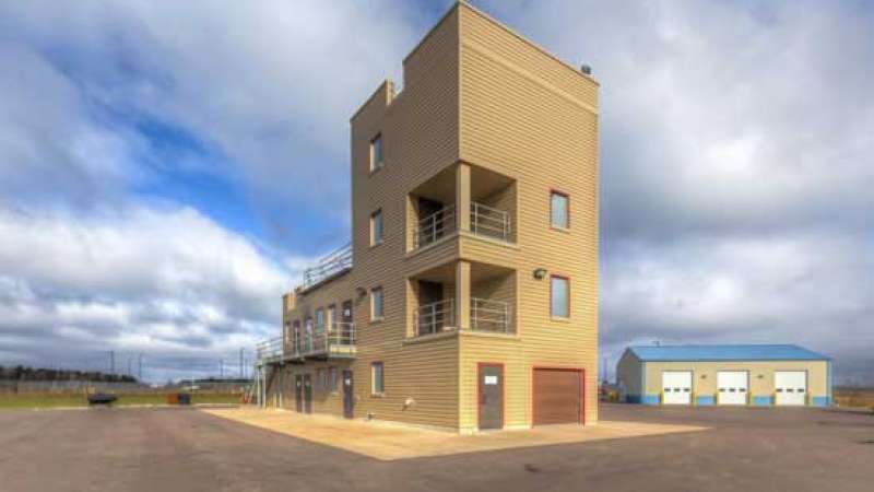 A tall burn tower with several open and enclosed areas stands with open pavement around it.