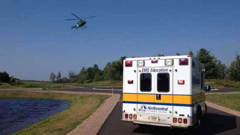 A water rescue area with an ambulance parked in the foreground and a helicopter flying overhead.