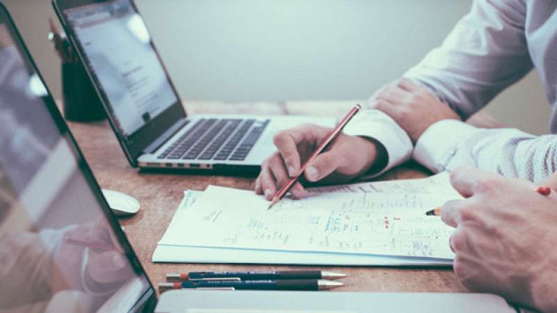 Financial advisors at a wide desk are looking over financial information on their laptops