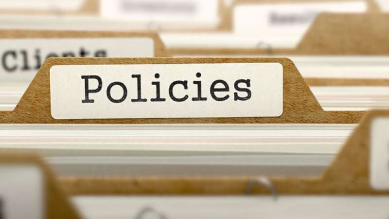 Several file folders are lined up with an emphasis on the word Policies labeled on a tab
