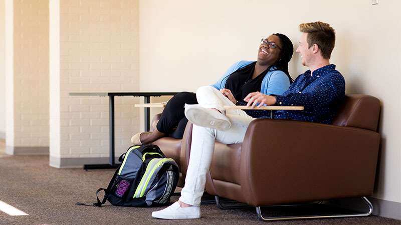 Two students are sitting down talking and laughing together