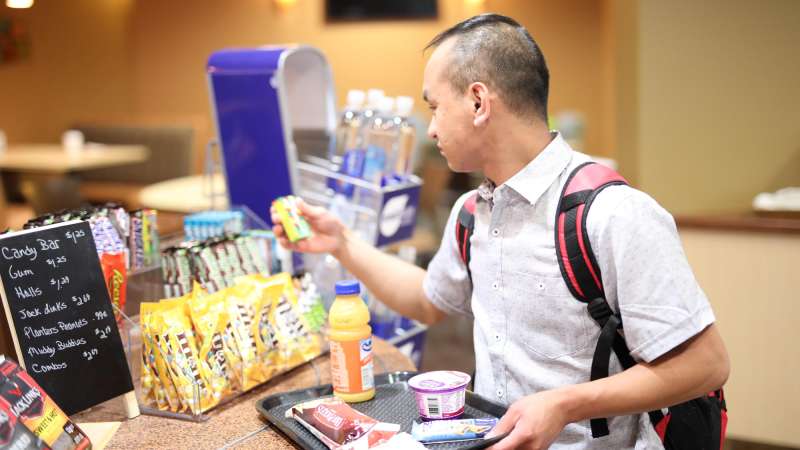 A student with a tray full of food picks up a pack of gum as he nears the cash register.