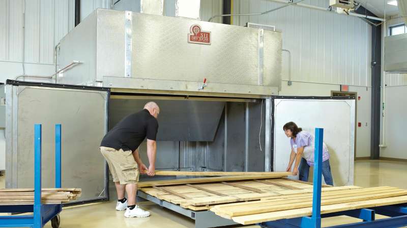 Two students load lumber into a dry kiln.