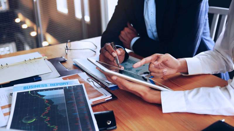 Two business people looking at an iPad, as business reports lay on the table in front of them.