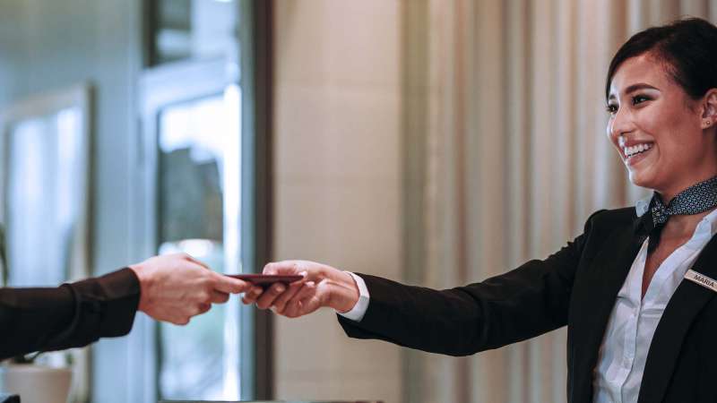 A woman working at a front desk handing over a hotel keycard and other information.