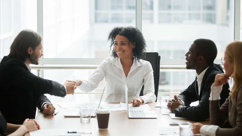 A group of business people sitting around a conference table, shaking hands and talking.