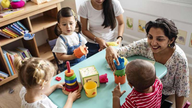 An early childhood teacher interacting with a group of young children at a table.