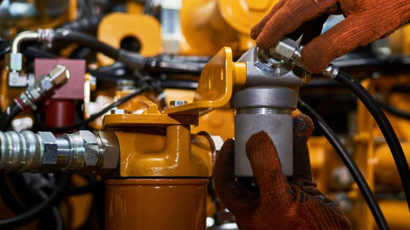 A lubrication specialist is connecting hoses to a machine inside of an industrial factory.