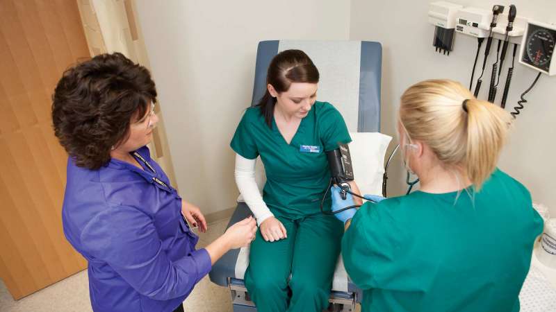 Two Medical Assistant students practicing their skills as an instructor looks on.