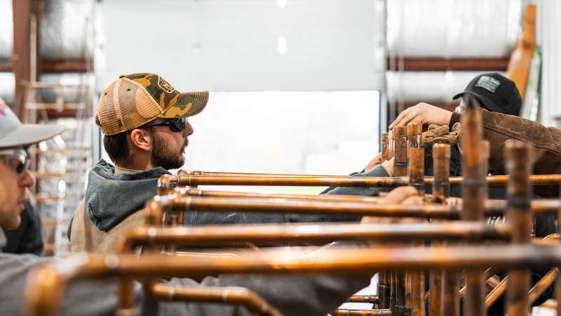 An apprentice is being shown how to create metal plumbing pipes.