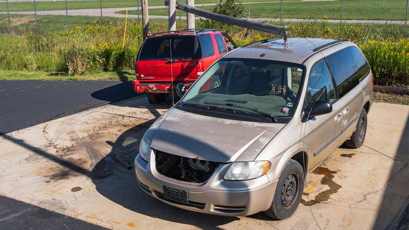 A utility pole with power lines are on top of a red SUV and a beige colored minivan.