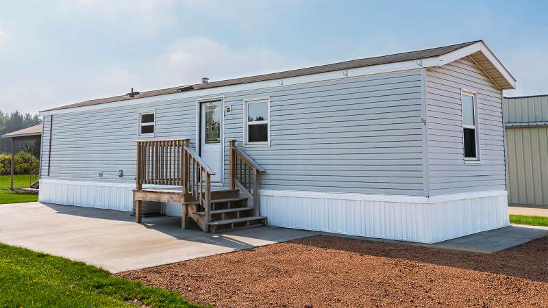 A light blue and white, small family mobile home with wooden stairs leading up to a door with a glass window.