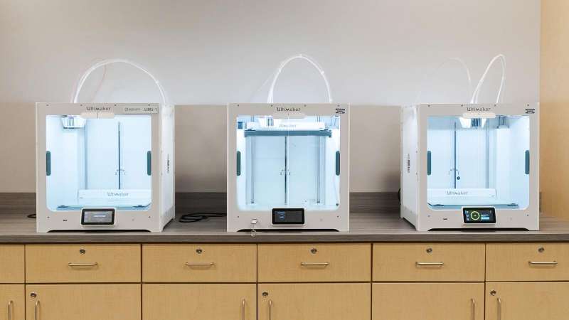 Three Ultimaker 3D printers sitting on a countertop, not currently in use.