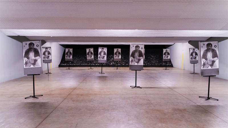 An indoor shooting range with several standing targets featuring a picture of an armed criminal on each one.