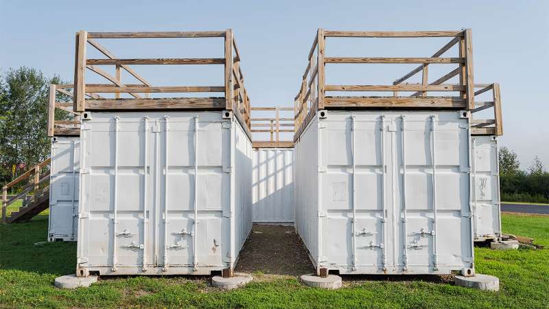 Two conex shipping containers are positioned side by side with a gap in-between to simulate a trench above the ground.