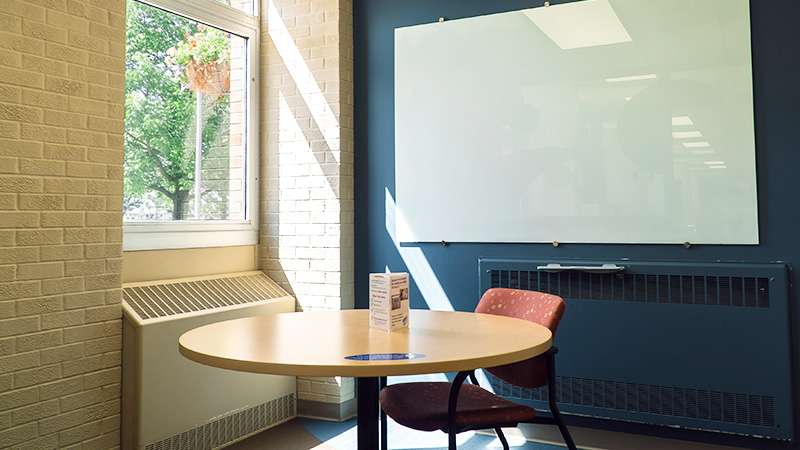 An internal view of a quiet study area with a round table, a white board, and a window letting lots of light in.