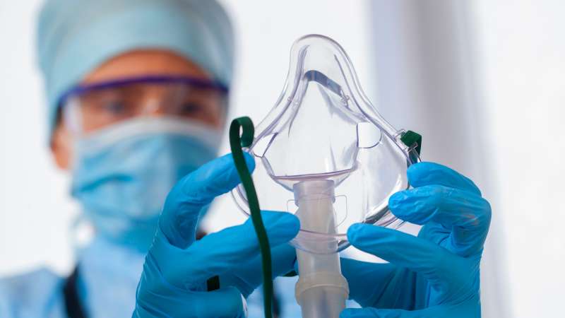 A respiratory therapist wearing medical exam gloves holds up a ventilation mask.