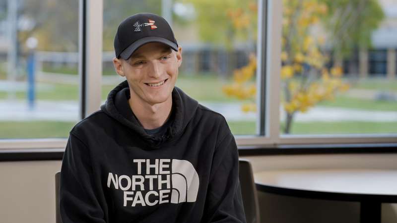 Brady Tlusty, a Plumbing Apprentice, sitting in front of several windows and smiling while talking about his apprenticeship experience.