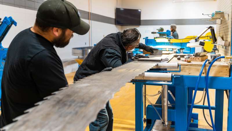 two men using equipment to sharpen teeth on a band saw blade