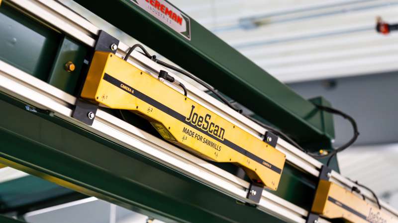 Detailed view of a JoeScan scanner system labeled: Made for Sawmills, mounted to a green Cleereman frame, used for precise log scanning and measurement.