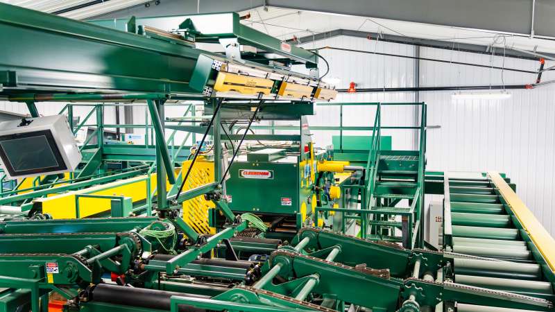 Overhead view of a Cleereman scanning and sorting line with mounted JoeScan log scanners, rollers, and monitoring equipment inside the sawmill training center.